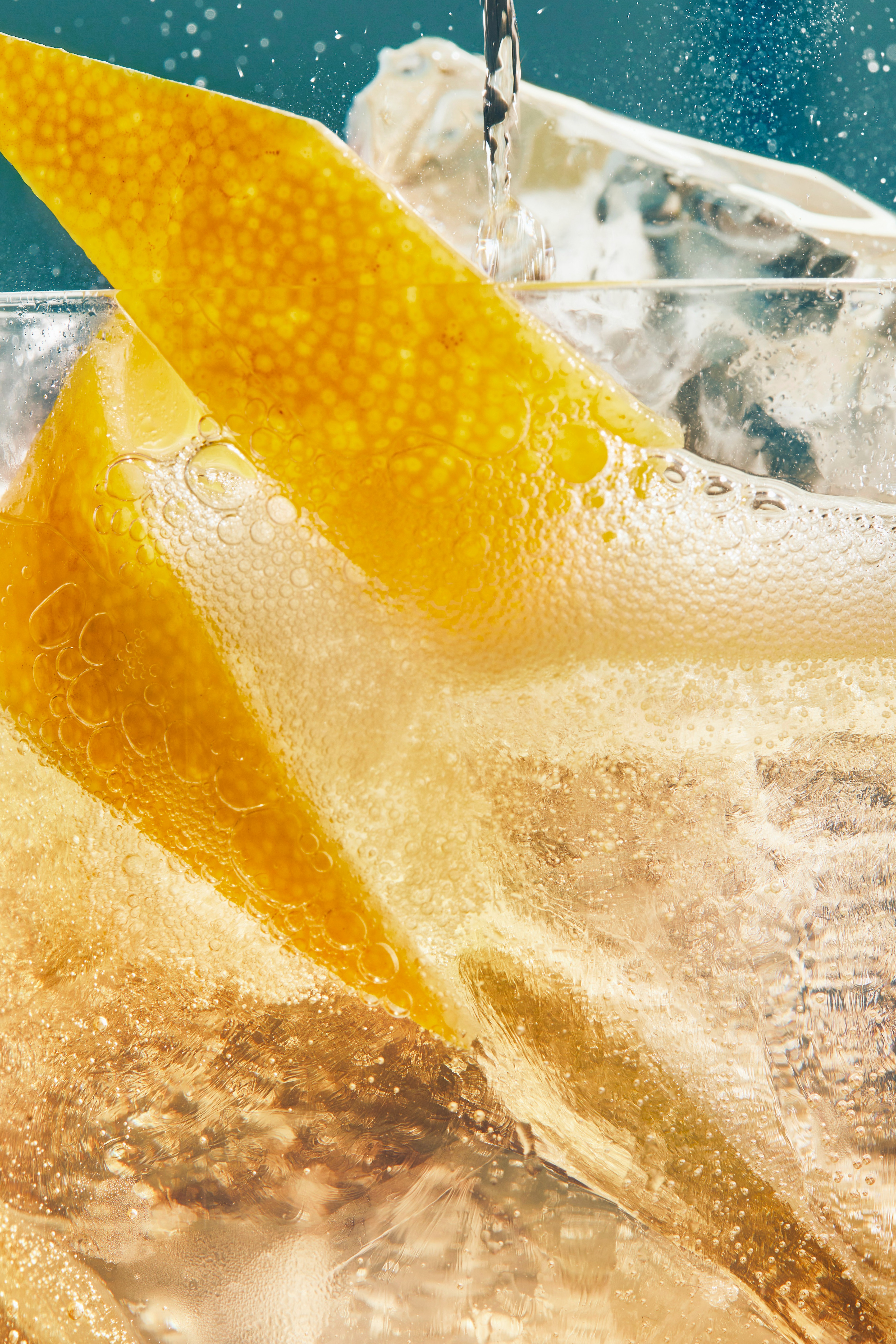 A close-up of a whisky cocktail containing ice and a lemon twist, with a bubbly liquid being poured into the glass.