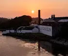 Een foto van de Lagavulin distilleerderij terwijl de zon ondergaat in de baai