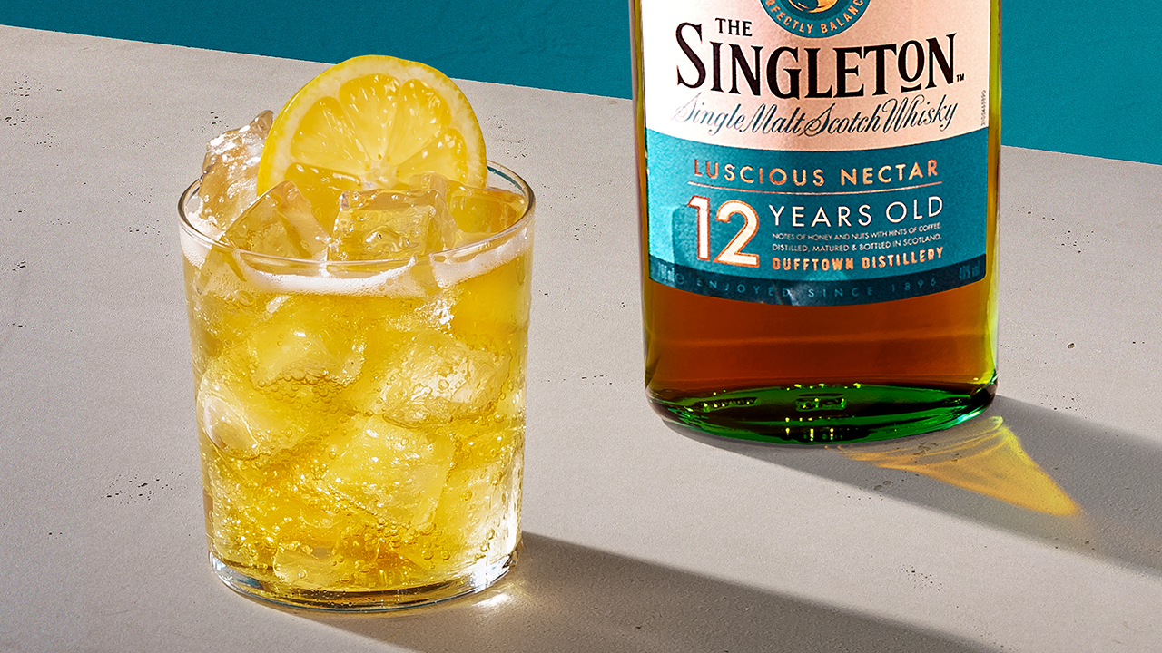 A yellow whisky cocktail next to a bottle of The Singleton 12-Year-Old Single Malt Scotch Whisky.