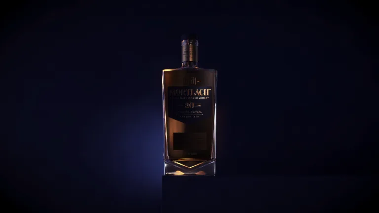 A bottle of Mortlach single malt Scotch whisky sits on a plinth in front of a gold and blue background.