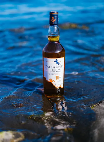 Eine Flasche Talisker 10 Jahre alter Whisky steht an einer Küste mit dem Meer im Rücken