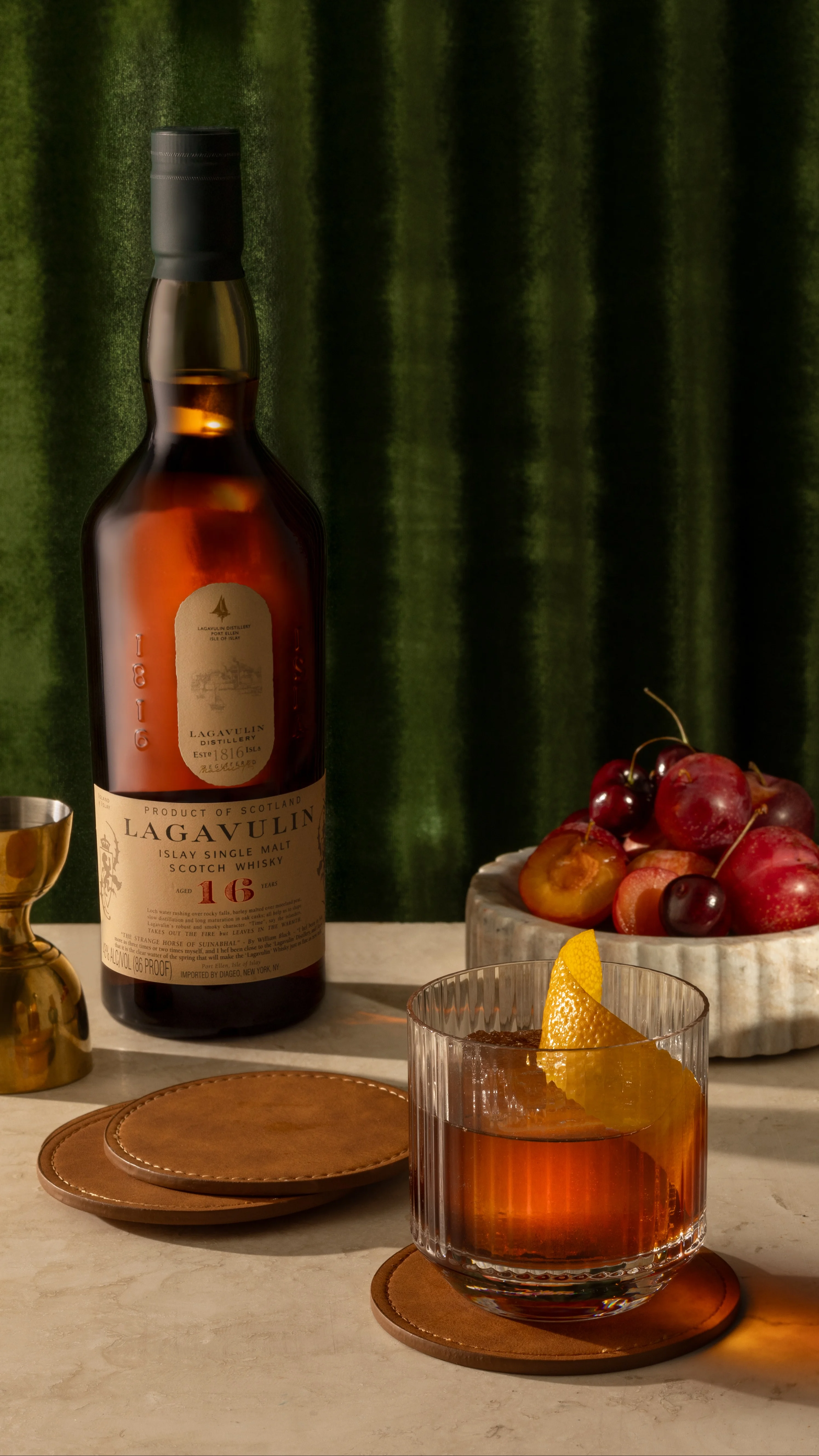 A cocktail next to a bottle of Lagavulin 16 and bowls of fruit