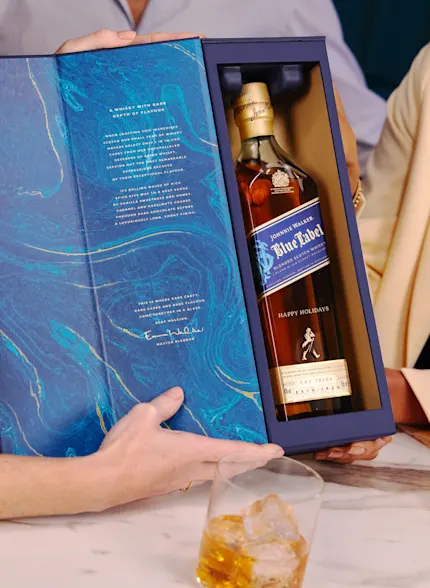 A bottle of Talisker 10-Year-Old Single Malt Scotch Whisky on a blue and beige background. A gold "Thank You" message is engraved on the bottle near the base.