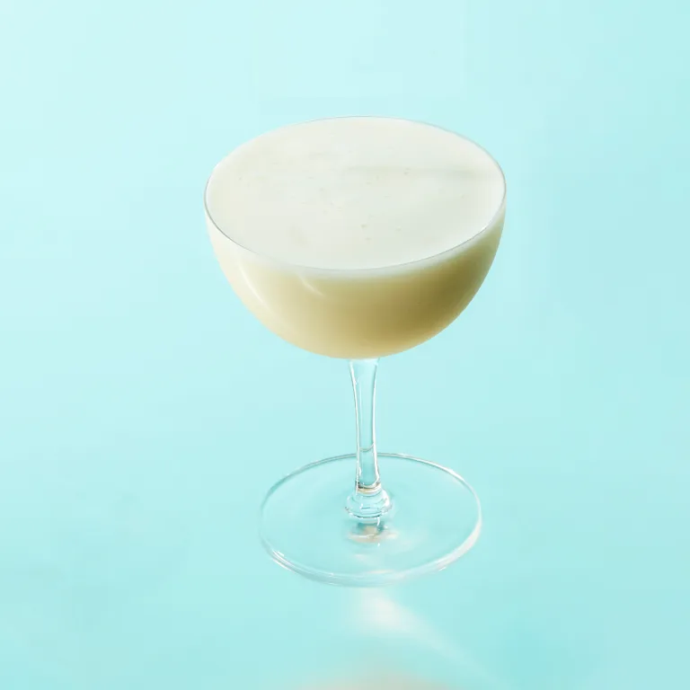 Een coupeglas met een schuimende drank tegen een bleke achtergrond.  