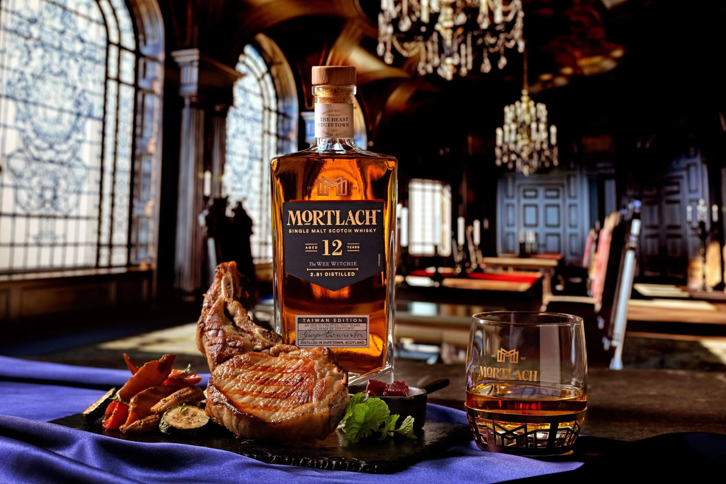 一瓶和一杯 Mortlach 12 年的 The Wee Witchie 放在桌上，旁邊有切片和方塊狀的豬五花。