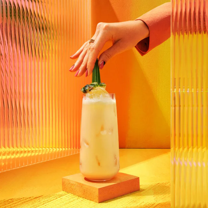 A hand places a pineapple garnish on a Johnnie Walker Salted Toffee Piña Colada cocktail.
