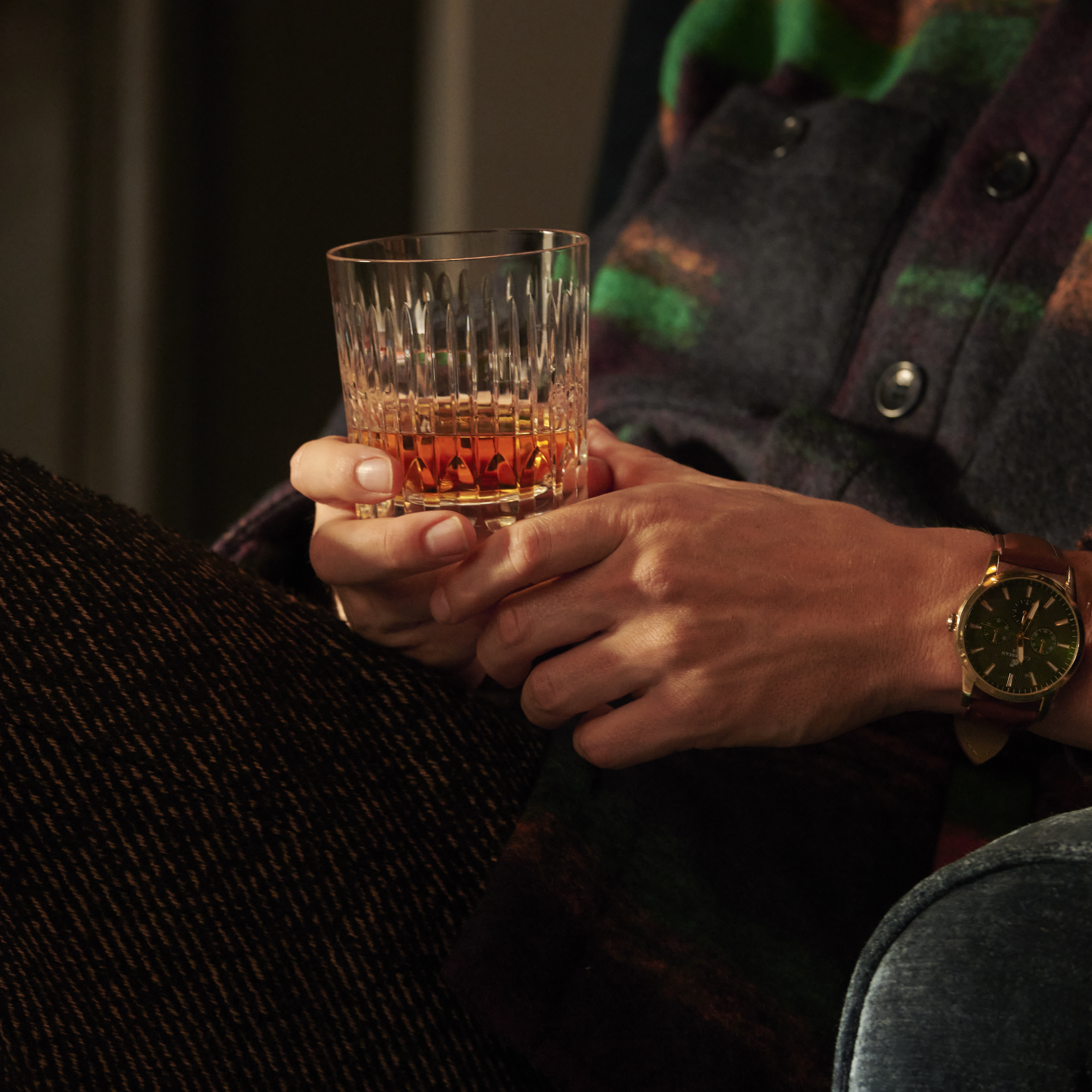 A man holds a rocks glass of neat whisky on his lap