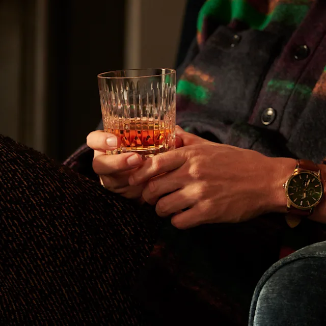 A man holds a rocks glass of neat whisky on his lap
