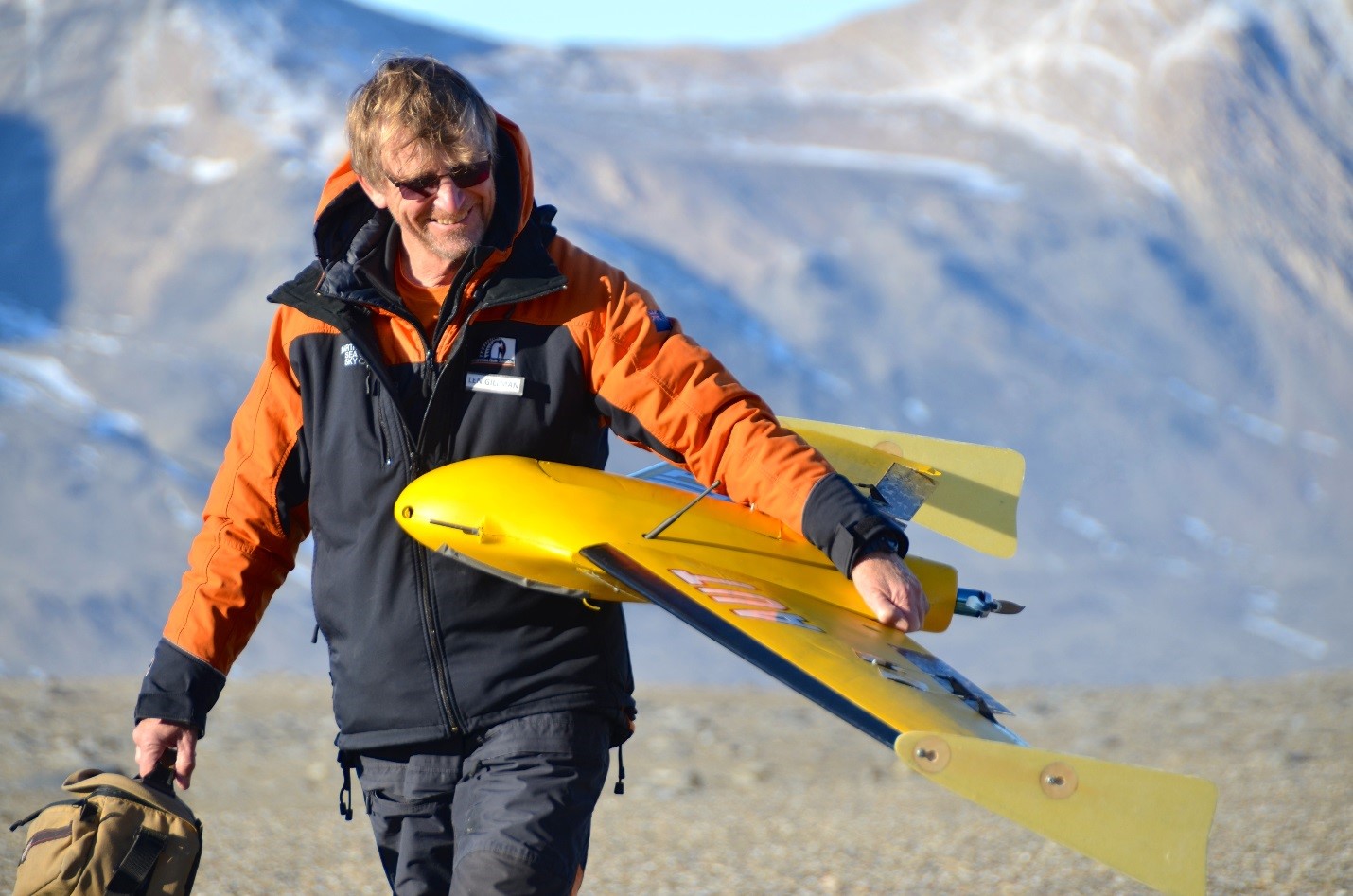 Len carrying a yellow drone labled AUT in Antarctica.