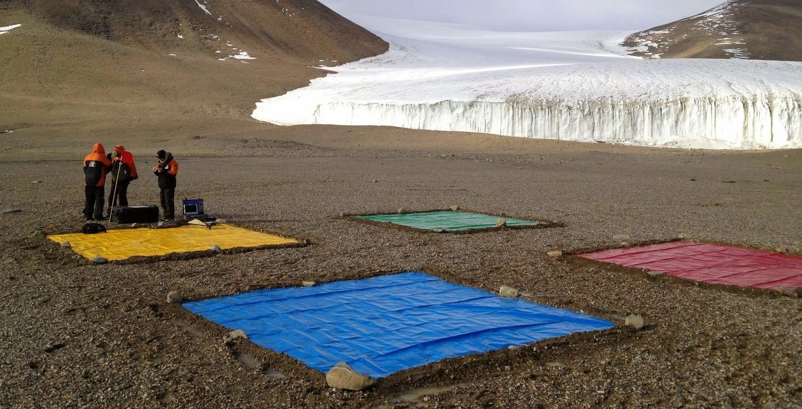 Four large coloured mats on a stony ground in Antarctica as a team prepares a drone for flight.