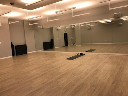 CPY studio room with tannish-gray hardwood floors and a single black CorePower Yoga instructor mat in the front center of the room