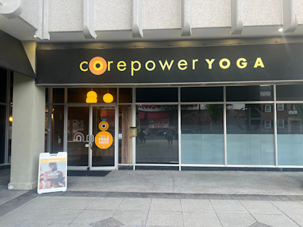 CorePower Yoga sign with yellow lettering on a black awning over a windowed wall of a grey concrete building 