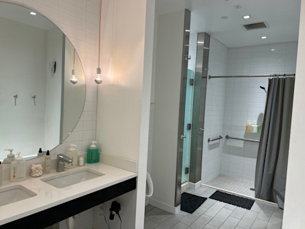 Locker room area with duel sinks and a large white tiled shower with a grey shower curtain