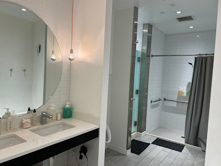 Locker room area with duel sinks and a large white tiled shower with a grey shower curtain