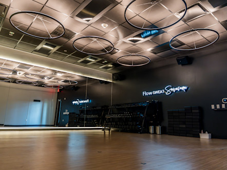 CorePower Yoga studio with mirrored wall, wood floor, circular ceiling lights, and blue neon “Flow SWEAT Savasana” sign