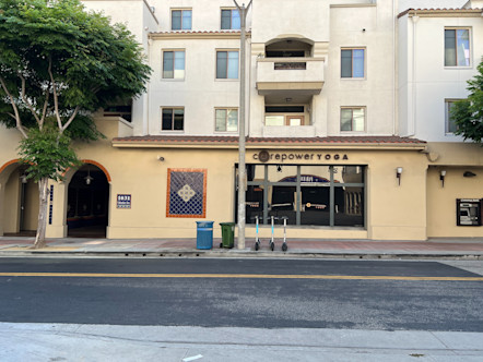 Single story tan stucco, Spanish style CorePower Yoga building with arched doorways below a white stucco apartment complex