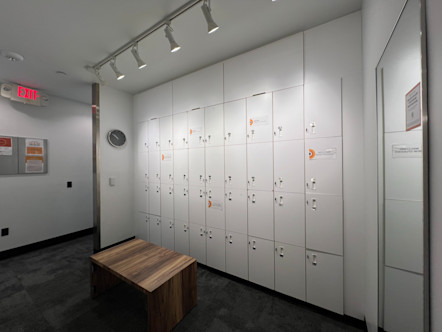 USC Village CPY locker room with four rows of white lockers and a wooden bench in front of them