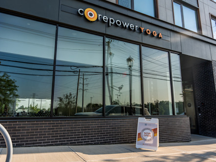 CorePower Yoga storefront with large glass windows and a sidewalk sign reading “Now Open” in front