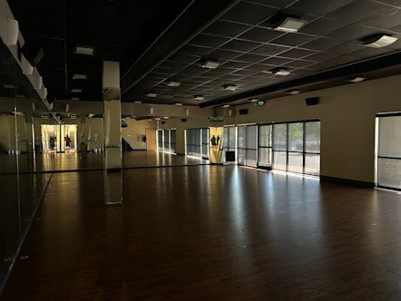 Dimly lit Mission Viejo practice room with dark brown wooden floors and pale yellow/mirrored walls 