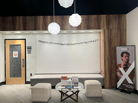 Lobby area with wooden paneled walls and a centered white textured wall with a string of polaroid photos hanging across it with a light grey bench underneath