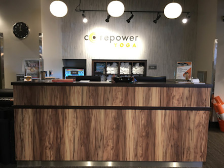 CorePower sign displayed on a white textured wall behind a warm wooden receptionist desk