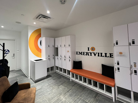 Emeryville CPY logo on white walls above an orange bench with white lockers surrounding on either side