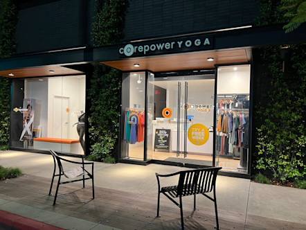Fully windowed CPY studio front with a white-light CPY sign above double glass doors and greenery surrounding the building front