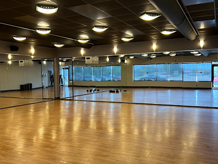 CPY studio room with light wash brown wooden floors, mirrored front and side walls, with sheer black window treatments over the back walls