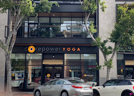 CorePower Yoga San Mateo studio's CorePower logo touted on black awning on exterior of building with green trees