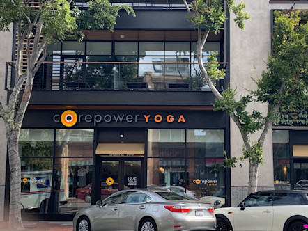 CorePower Yoga San Mateo studio's CorePower logo touted on black awning on exterior of building with green trees