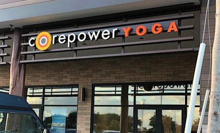 CorePower Yoga sign displayed on metal bars arched above a tan brick building with glass entrance doors
