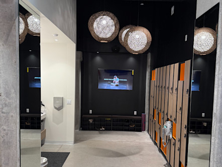 Mueller CPY studio hallway with light tan and orange lockers to the right, locker room entrances to the left, and a digital screen at the end of the hall in the center