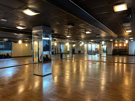 CPY studio room with rich wooden floors, black paneled ceilings, and front and side fully mirrored walls with a mirrored column in the center