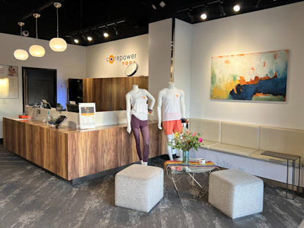 CorePower Yoga front lobby with a large L-shaped wooden desk in the back corner and a seating area with creme couches and ottomans in front
