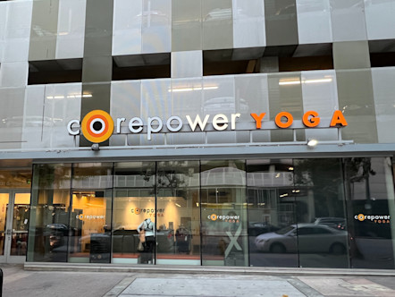 White and orange colored lettering in a large CorePower Yoga sign above a fully windowed entrance on the ground floor of an office building