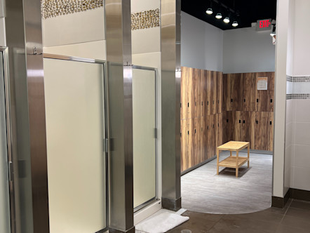 Woodbury studio locker room with three showers side by side, each with frosted glass, and a back room with wooden, double layered lockers