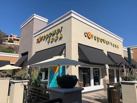White and tan building with black awnings touting a yellow and orange CorePower Yoga sign