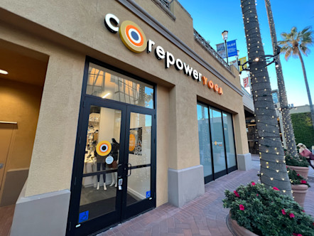 White and orange CorePower Yoga sign on a yellow stucco building with palm trees and flowerpots in front