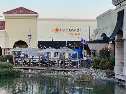 CorePower yoga sign displayed above a black awning with a group of umbrellas out front and a mid size pond