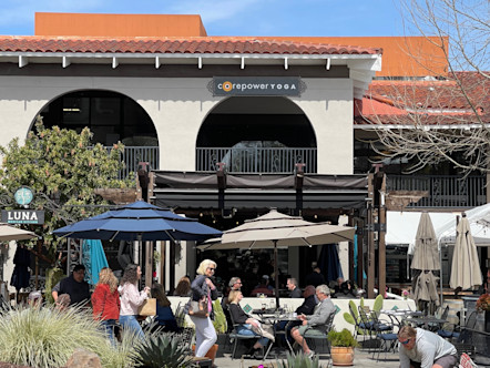 CorePower Yoga sign displayed on the second floor of a white tuscan looking building with red roofing and umbrellas out front