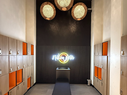 Modern locker room with wooden and orange lockers, pendant lights, bench seating, and neon CPY sign on dark wall