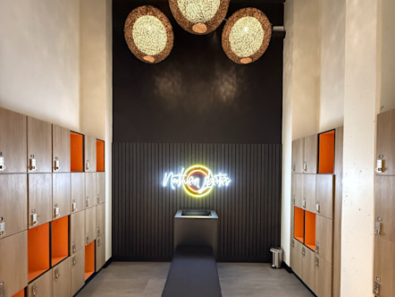Modern locker room with wooden and orange lockers, pendant lights, bench seating, and neon CPY sign on dark wall