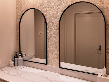 Modern bathroom vanity with marble countertop, two arched mirrors, pebble-tile wall, and white pendant lights.