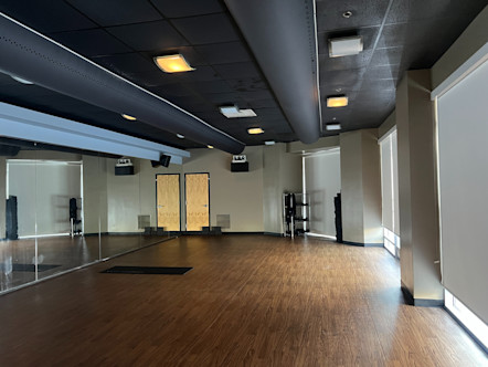 CPY studio room with medium brown wooden floors, light tan colored walls, and floor to ceiling windows in the back