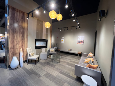 Gray couch with orange throw pillows and two white accent chairs surrounding a stone fireplace