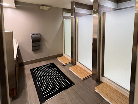 Three identical CPY showers with frosted glass doors and light wooden paneled mats in front 