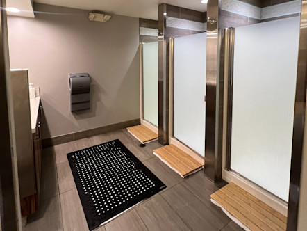 Three identical CPY showers with frosted glass doors and light wooden paneled mats in front