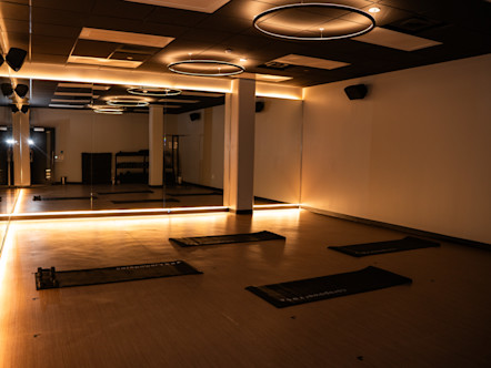 Modern CorePower Yoga studio with warm lighting, circular ceiling fixtures, mirrored wall, and exercise mats arranged on wooden floor