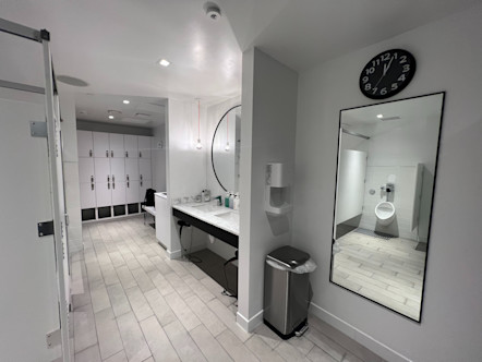 Fully white locker room with white and grey tiled floors and a white marbled vanity with a triple row of white cubbies and lockers