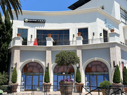 Black CPY sign on the second level of a white brick building with rounded entry ways and small shrubbery outside on the ground floor